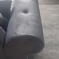 Close-up of a dark gray upholstered cylindrical ottoman or stool cushion with button tufting, shown on a carpeted floor.