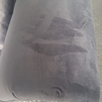 A close-up of a dark gray fabric cushion or upholstered furniture surface with visible wear, stains, or fading on the front panel.