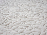 Close-up of a white quilted fabric with an intricate swirling floral pattern.