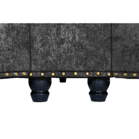 Close-up of a gray upholstered chair with black legs and gold studs on a white background