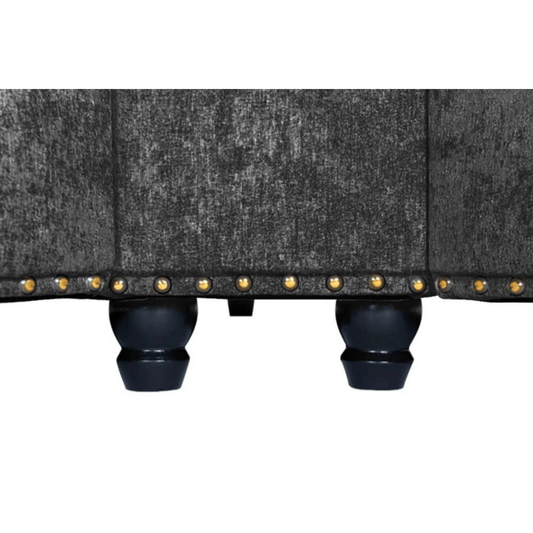 Close-up of a gray upholstered chair with black legs and gold studs on a white background