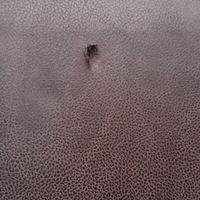 Close-up of a textured brown leather surface with a small hole.