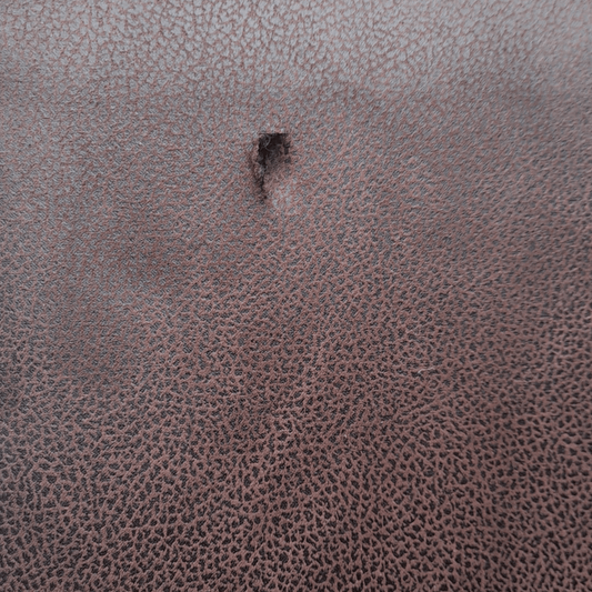 Close-up of a textured brown leather surface with a small hole.