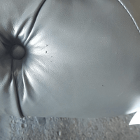 Close-up of a gray leather cushion with a button on a textured surface.