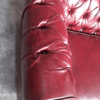 Close-up of a red leather sofa with tufted design on a gray floor.