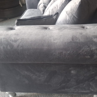 Close-up of a dark gray velvet or microfiber upholstered sofa section, showing the tufted armrest and side panel with visible wear marks and scuffs.