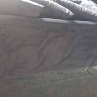 A close-up view of a gray upholstered bed frame with patterned gray bedding and pillows, resting on a gray carpeted floor.