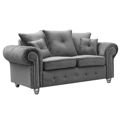 Grey velvet sofa with tufted backrest and decorative pillows on a white background