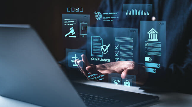 Hand holding a digital compliance icon with laptop and blurred background