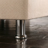 Close-up of a beige woven fabric upholstered furniture corner resting on a polished chrome metal leg over a dark tiled floor.