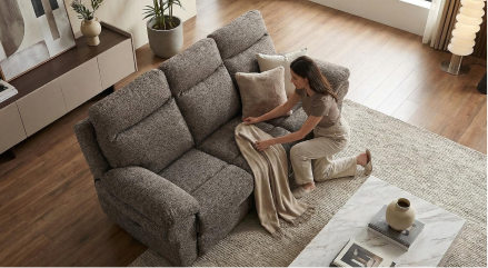 Woman arranging cushions on a gray sofa in a living room.