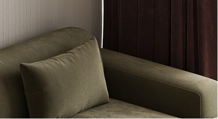 Brown sofa with a pillow against a neutral wall and dark curtains.