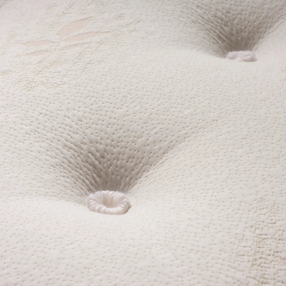Close-up of a white tufted mattress or upholstered surface with visible stitched button tufts and a textured dotted fabric pattern.
