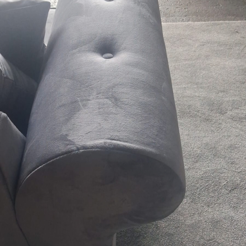 Close-up of a dark gray upholstered cylindrical ottoman or stool cushion with button tufting, shown on a carpeted floor.