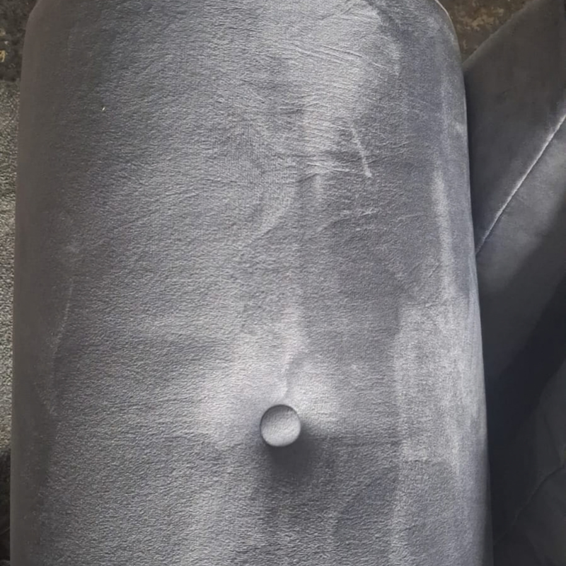 Close-up of a gray upholstered furniture piece, showing a tufted button and textured fabric surface.