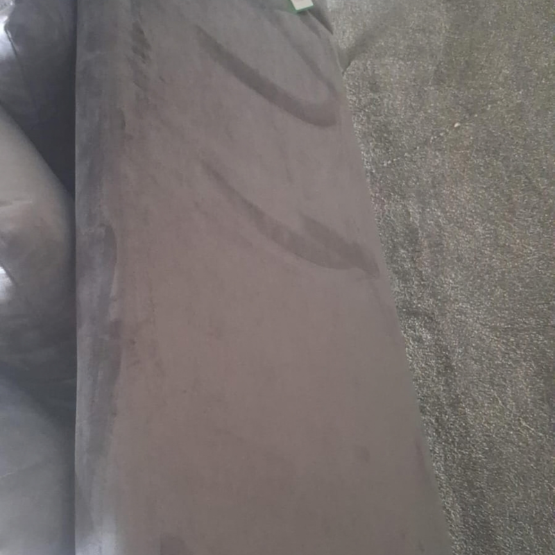 A close-up view of a dusty brown upholstered armrest or sofa section, showing visible scuffs and dirt marks on the surface, next to a textured gray carpet.