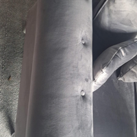 Close-up of a gray upholstered armchair or sofa section with tufted button details and a matching cushion, photographed indoors on a carpeted floor.