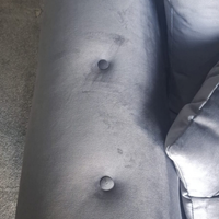Close-up of a gray upholstered armrest with two button tuftings and visible scuffs and stains on the fabric.