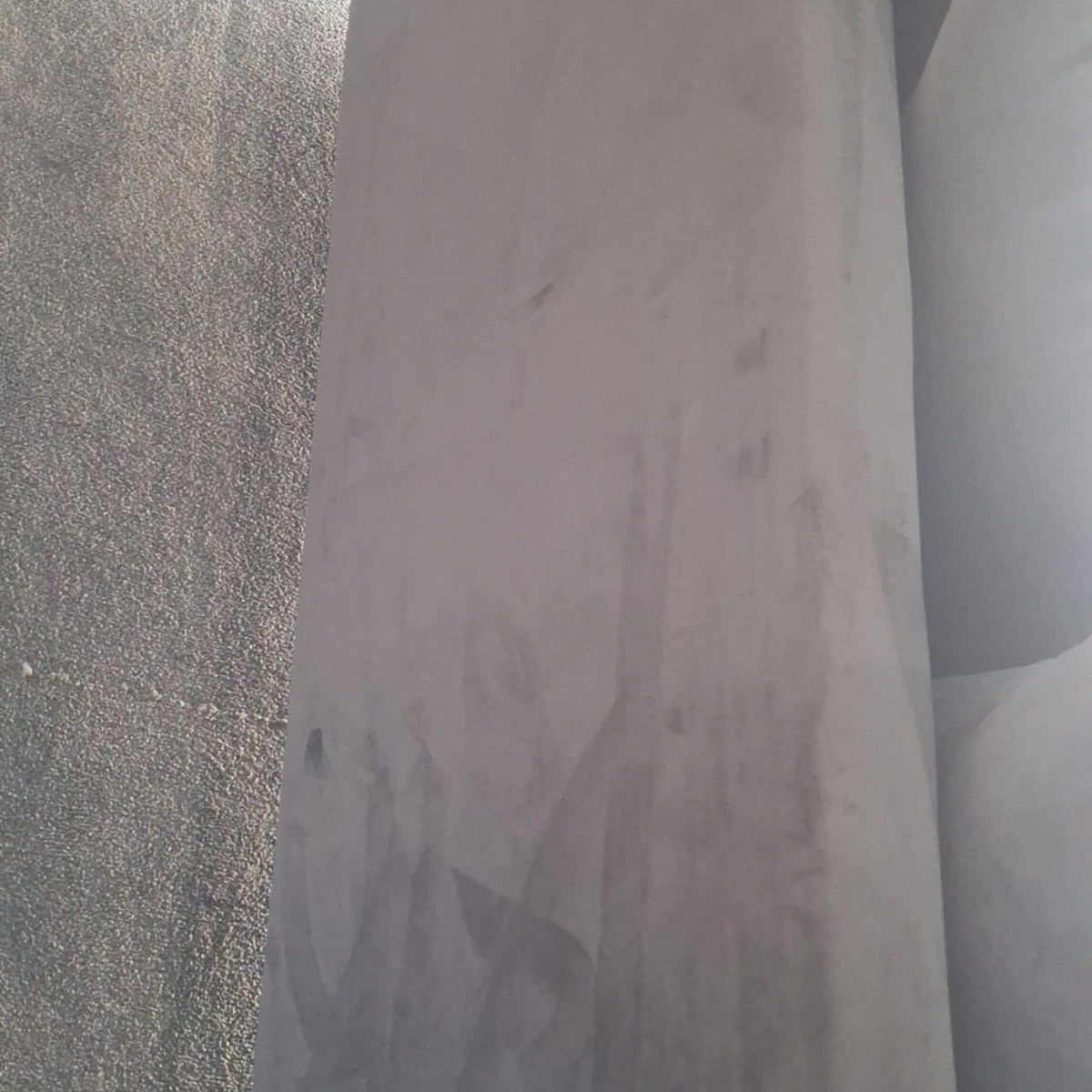 A close-up of a large, light gray sheet of material, possibly metal or plastic, standing vertically next to a textured gray surface.