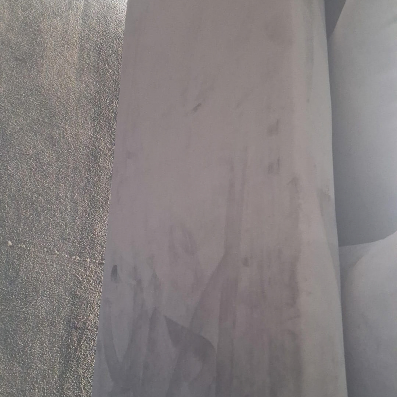 A close-up of a large, light gray sheet of material, possibly metal or plastic, standing vertically next to a textured gray surface.