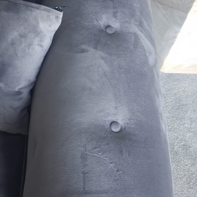 Close-up of a gray velvet upholstered furniture piece, showing a button-tufted surface and part of a matching cushion.