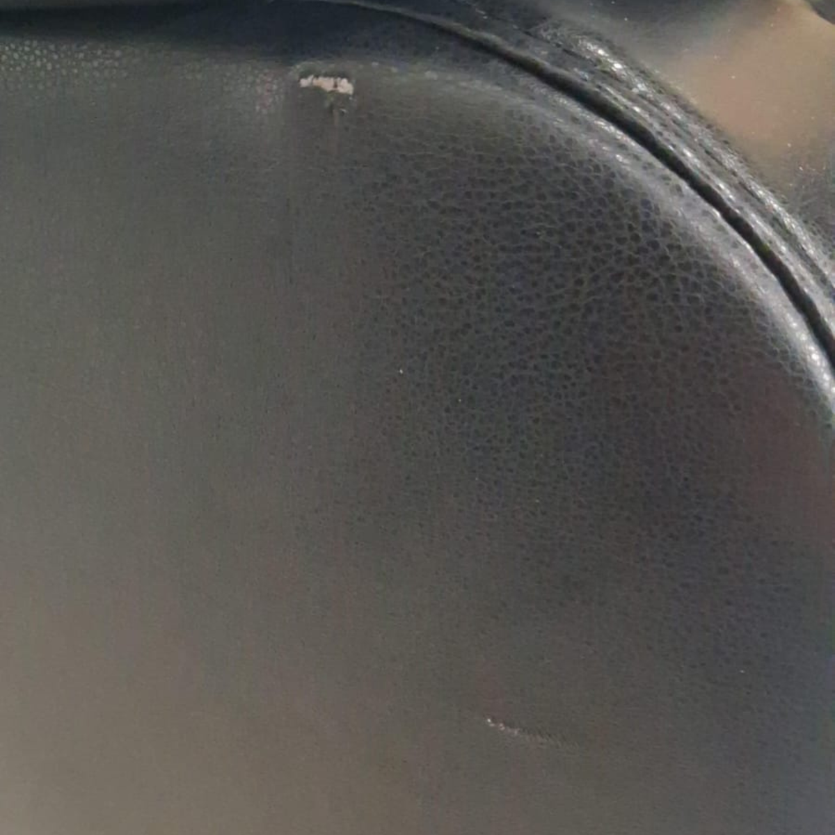 Close-up of a dark gray pebbled leather or faux leather surface with a curved seam and a small visible scratch near the top.