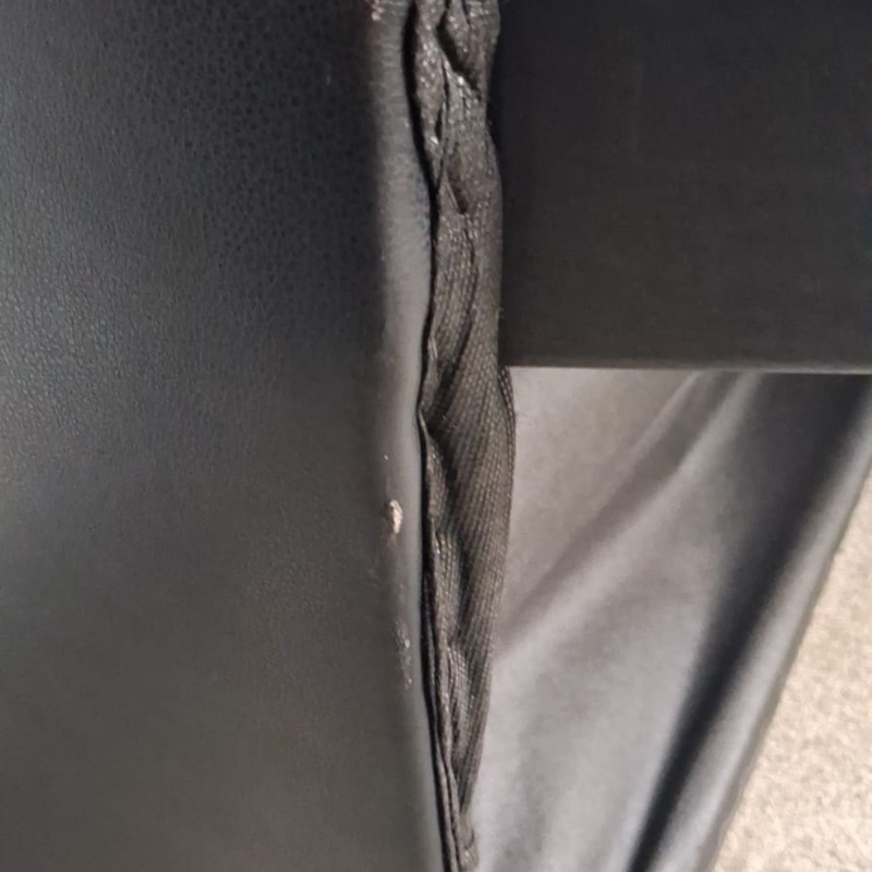 Close-up of a black faux leather or vinyl chair arm with a braided seam detail and a small scuff on the surface.