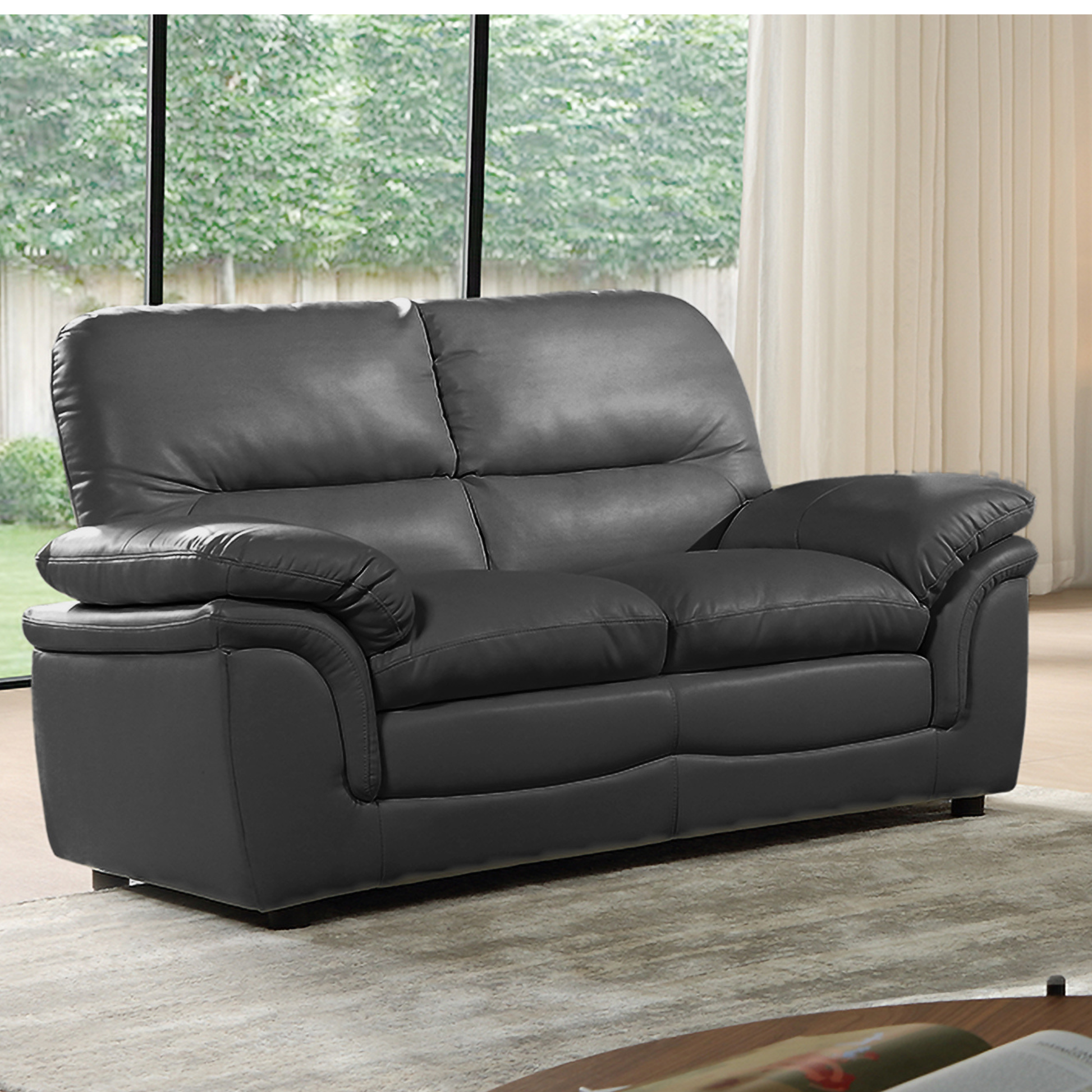 Gray leather sofa in a living room setting with large windows and curtains.