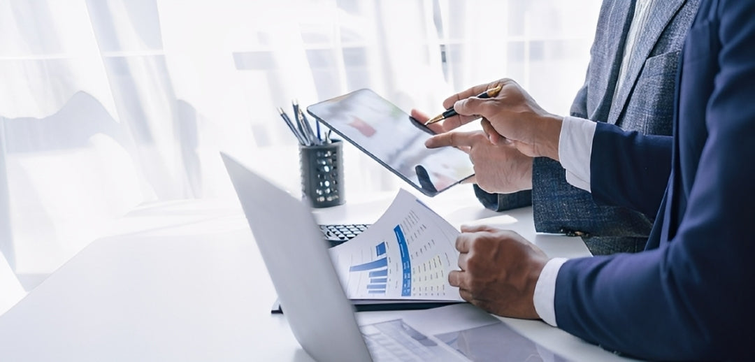 Person in a suit working on a laptop with documents and a tablet in an office setting