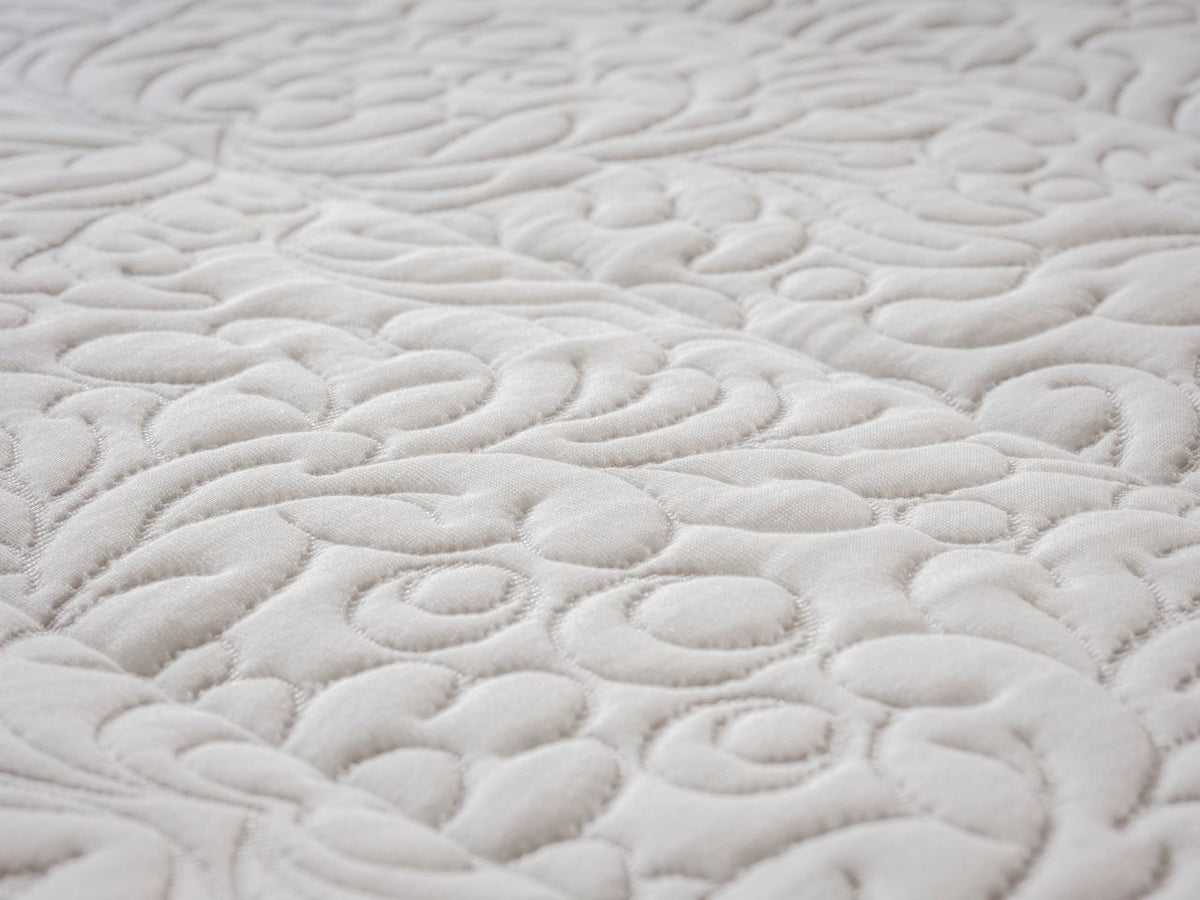 Close-up of a white quilted fabric with an intricate swirling floral pattern.