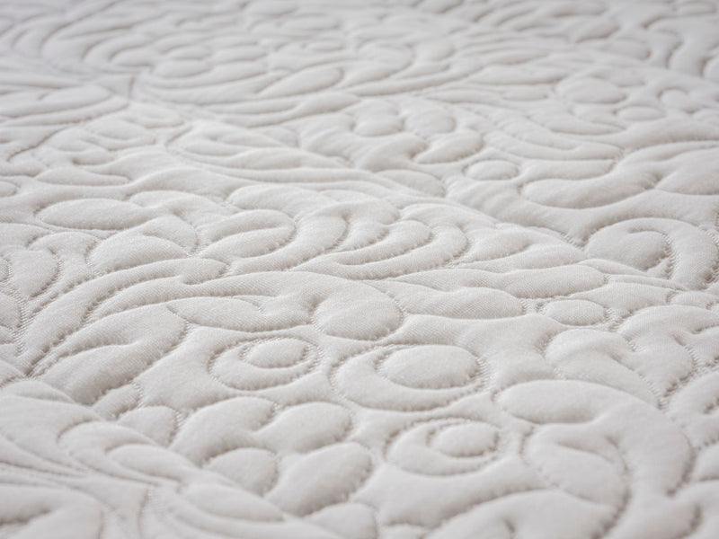 Close-up of a white quilted fabric with an intricate swirling floral pattern.