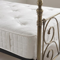 A close-up of a white tufted mattress on a bed frame with an antique brass metal headboard and footboard.
