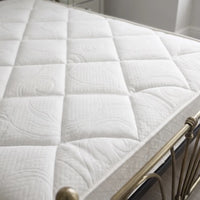A close-up of a white quilted mattress topper or mattress surface on a bed frame, with the bedding texture and diamond quilting pattern visible.
