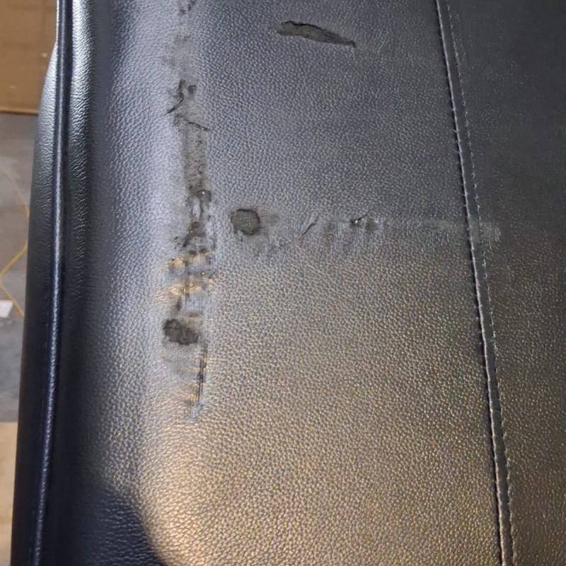 Close-up of a black textured leather or faux-leather surface with visible scratches, scuffs, and wear marks along a vertical seam.