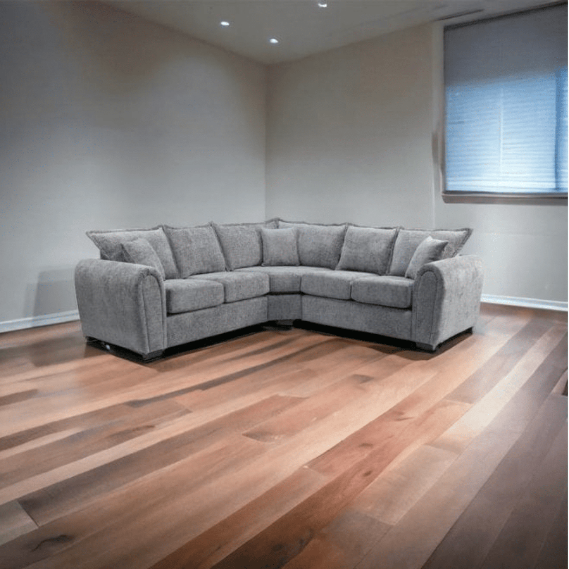 Gray sectional sofa in a room with wooden flooring and a window.