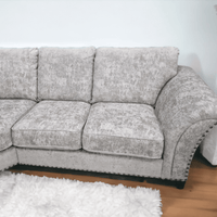 Gray sectional sofa with nailhead trim on a wooden floor.