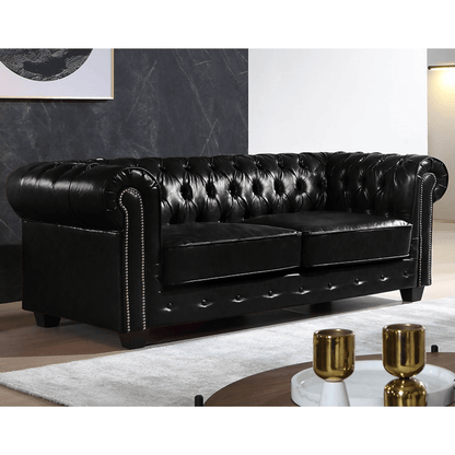 Black leather Chesterfield sofa in a living room setting with a coffee table and decor items.