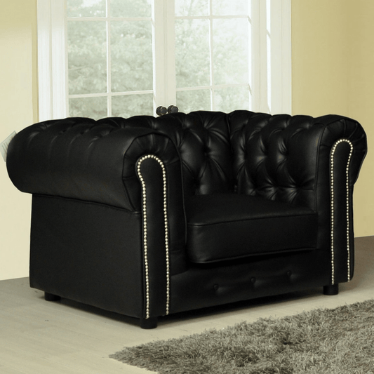 Black leather sofa with tufted backrest and nailhead trim in a room with large windows.