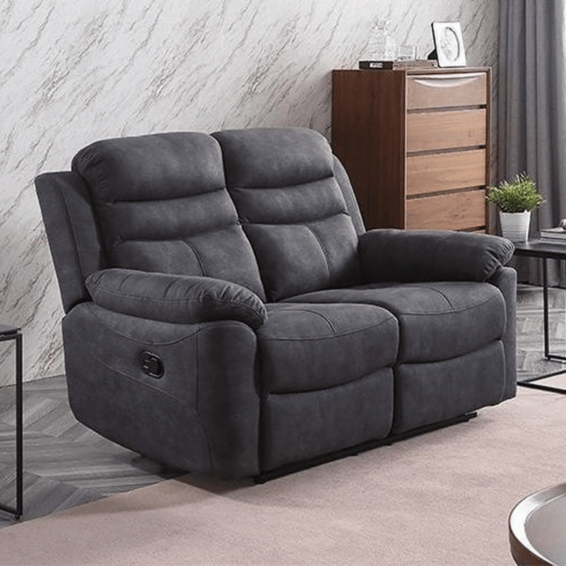 Grey recliner sofa in a living room setting with a wooden cabinet and plant in the background.