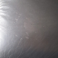 A close-up of a dark gray textured material, resembling leather or faux leather, with visible scuffs and scratches.