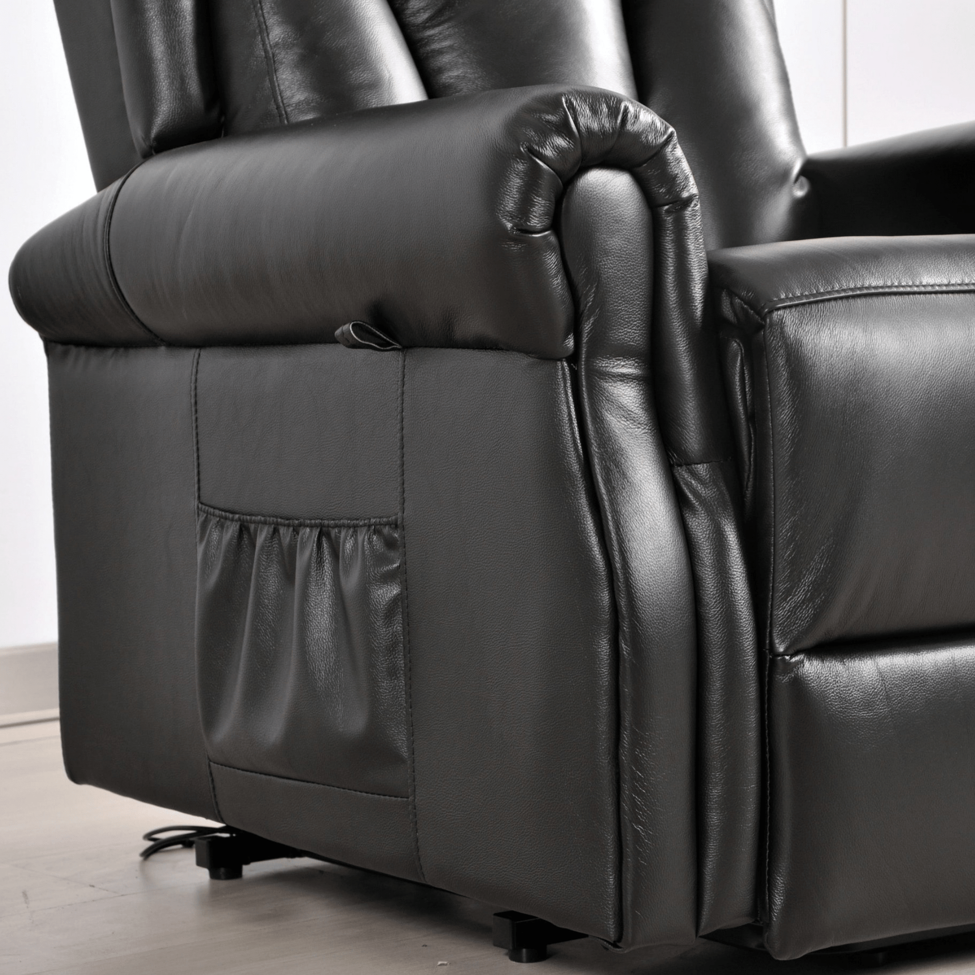 Close-up of a black leather recliner chair with power button on a light wooden floor.