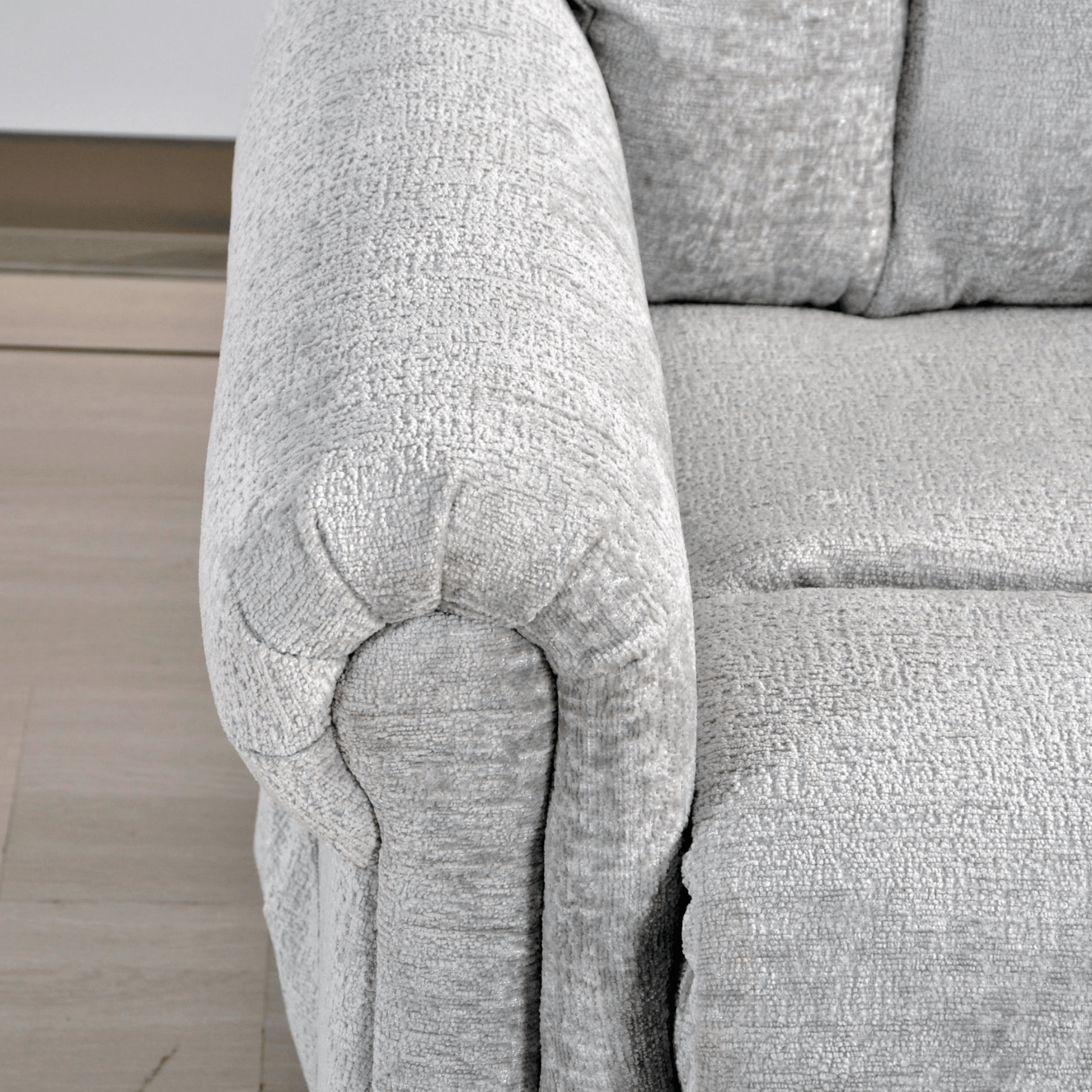 Close-up of a textured gray sofa armrest on a light wooden floor.