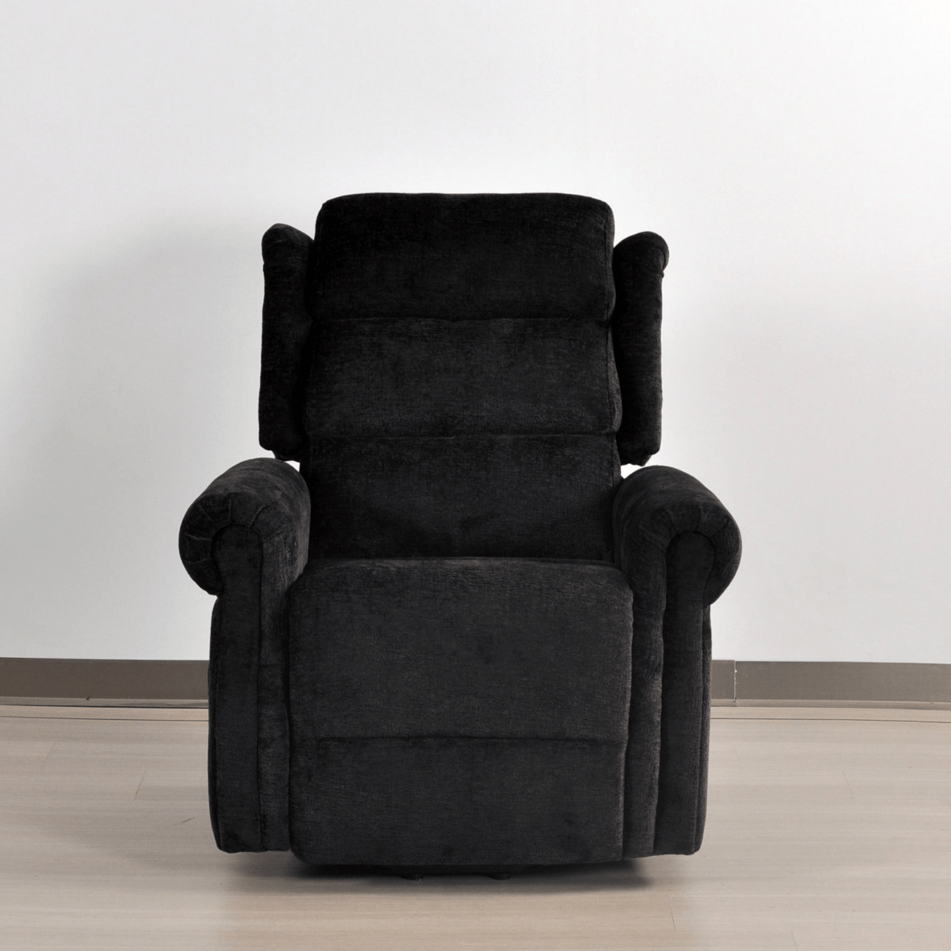 Black recliner chair on a light wooden floor with a white wall background