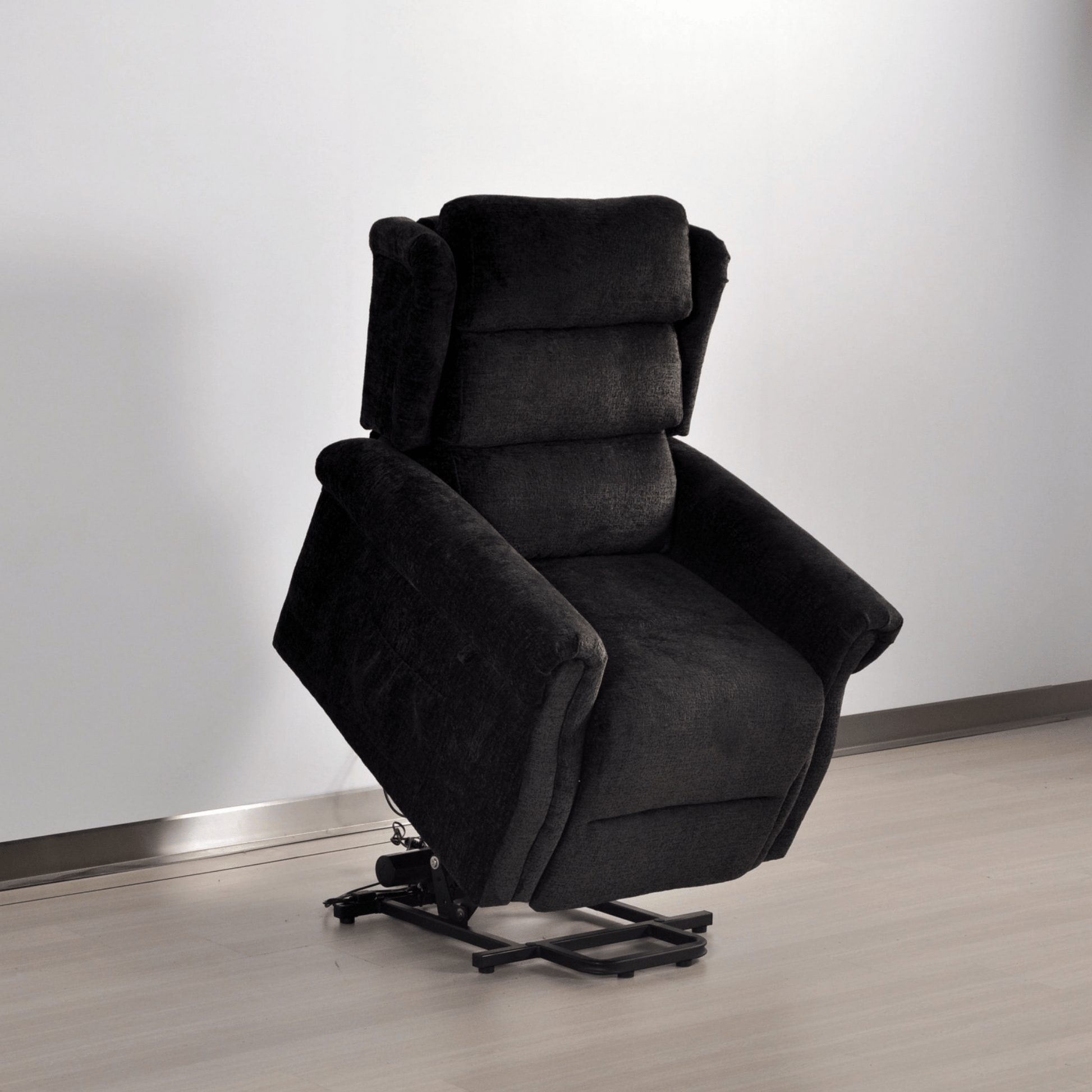 Dark gray recliner chair on a light wooden floor with a white wall background