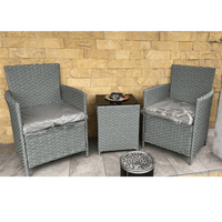 Two gray wicker chairs with cushions in front of a stone wall.