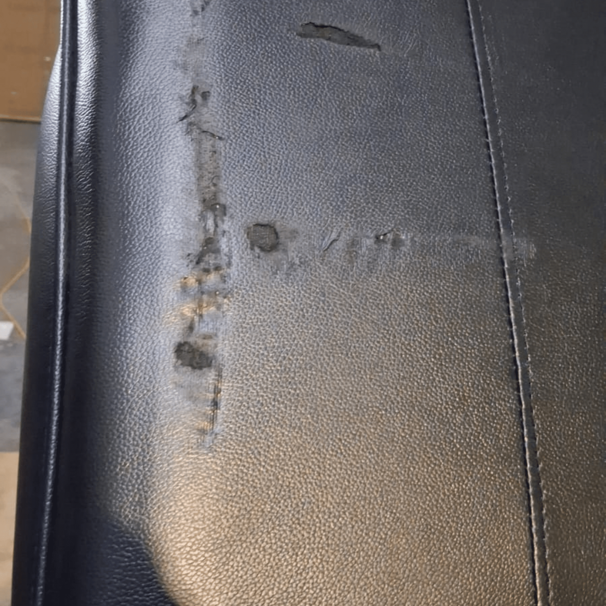 Close-up of a black textured leather or faux-leather surface with visible scratches, scuffs, and wear marks along a vertical seam.