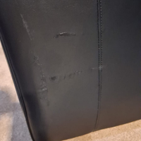 Close-up of a black leather or faux-leather upholstered surface with visible scuffs, scratches, and wear marks along a vertical seam.