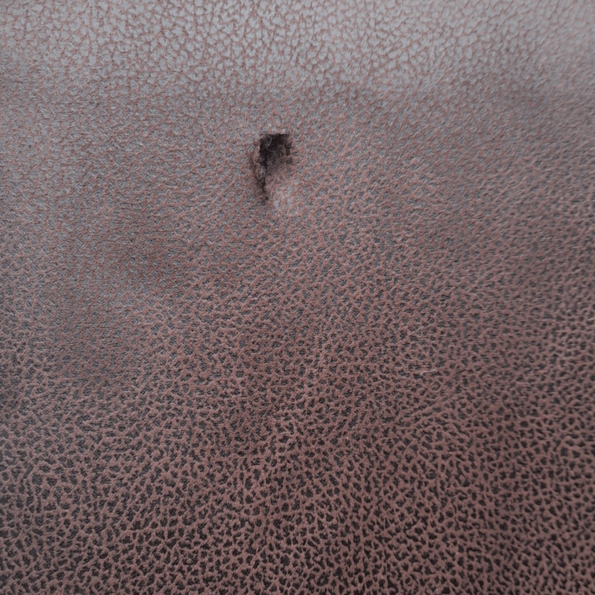 Close-up of a textured brown leather surface with a small hole.