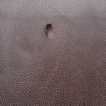 Close-up of a textured brown leather surface with a small hole.