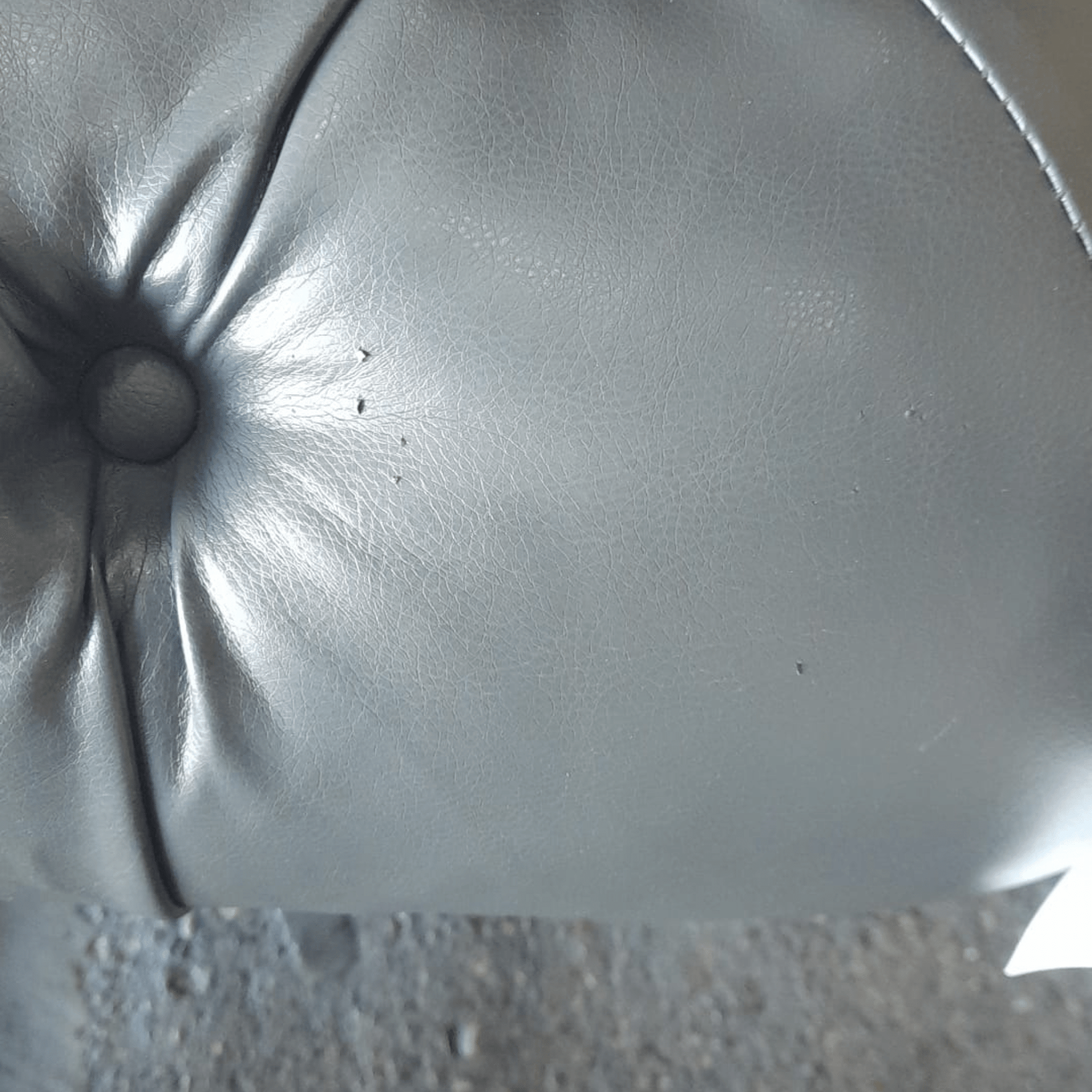 Close-up of a gray leather cushion with a button on a textured surface.